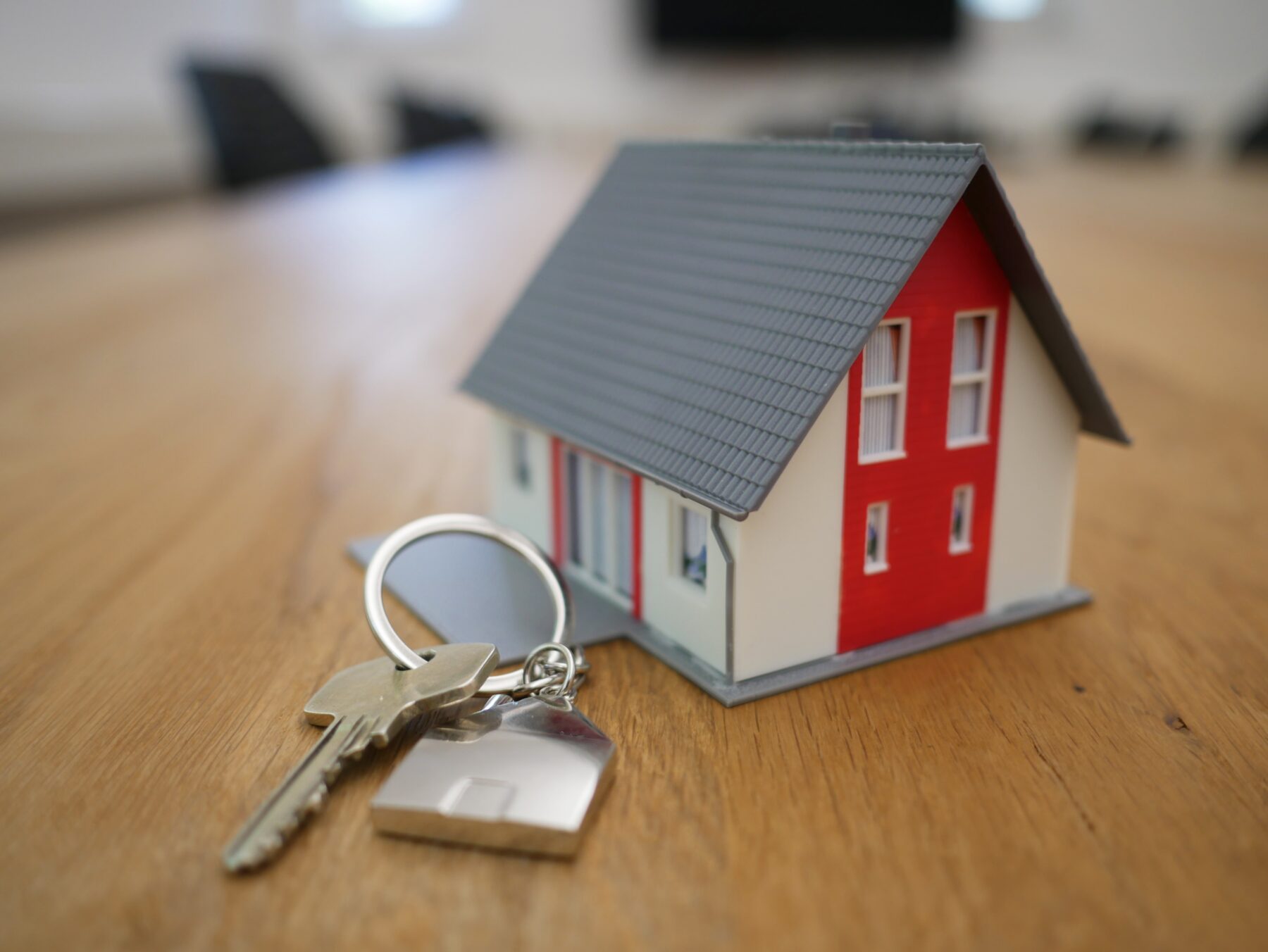 little red house model on table next to a metal key on a key chain