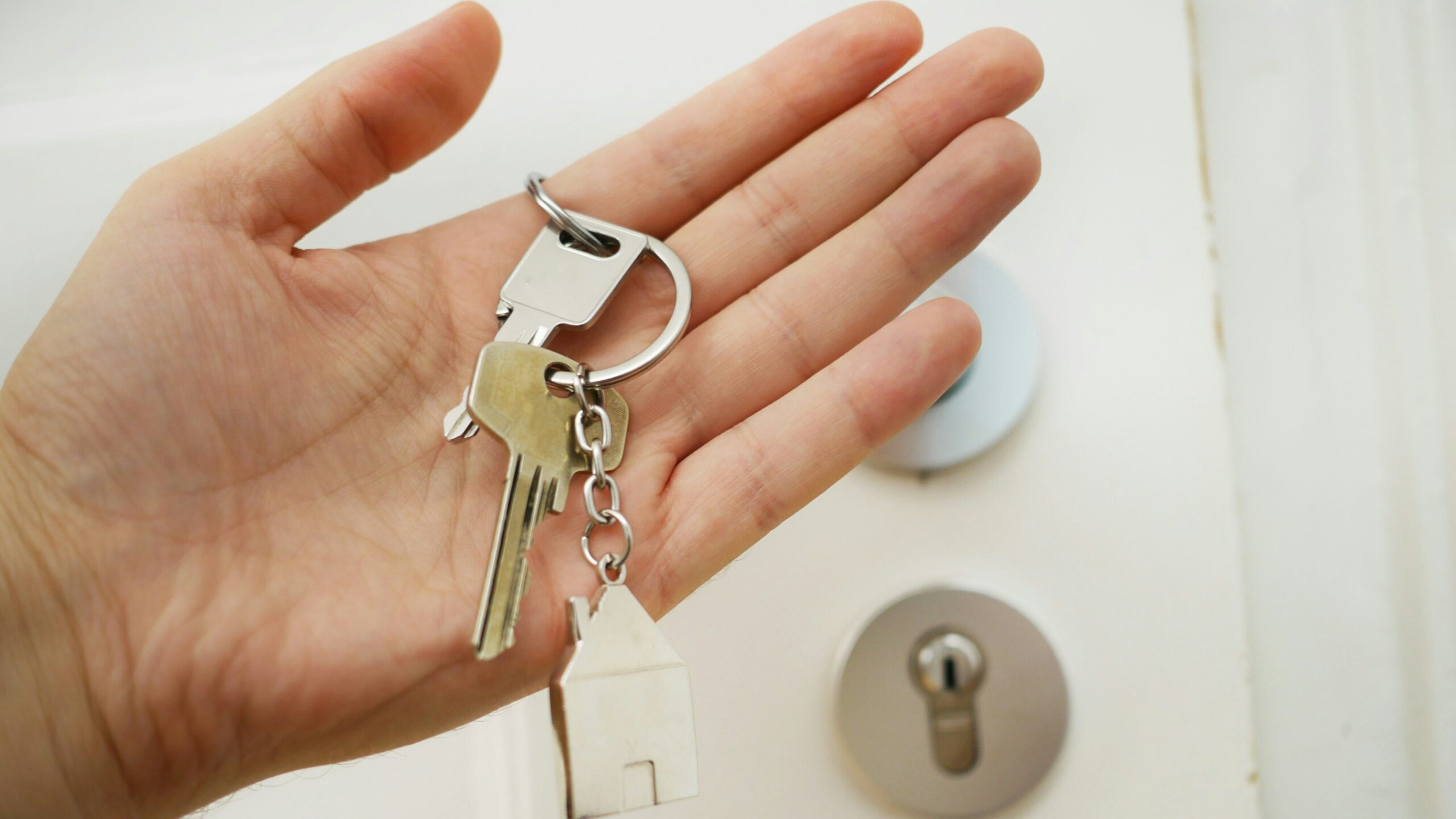cybersecruty in real estate a male hand holding a golden key chaing with two keys and a house figure in front of white door