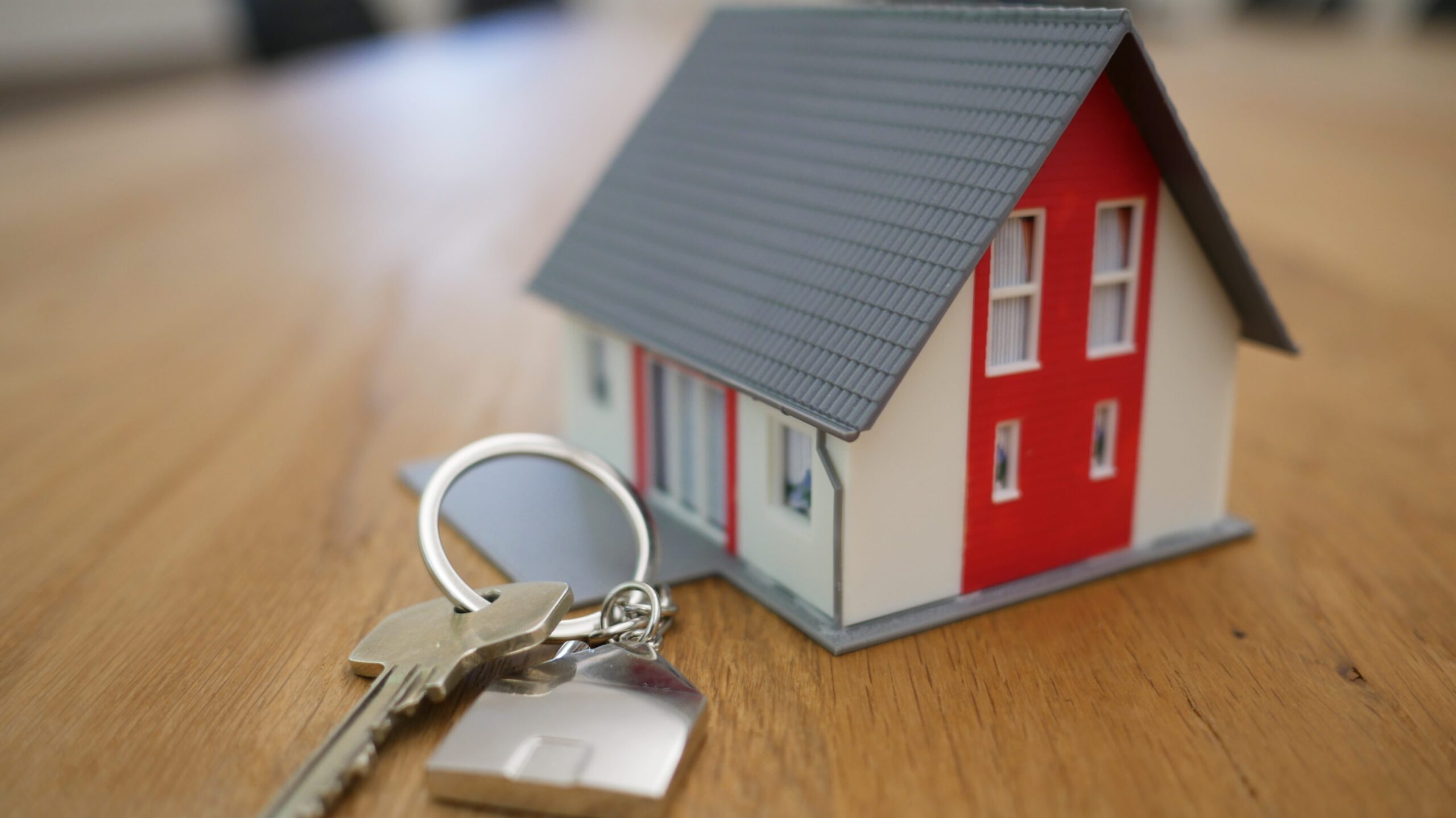 buyers agent commission- little red house model on table next to a metal key on a key chain